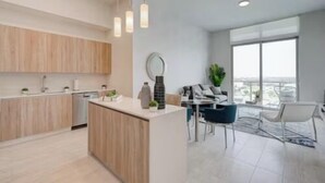 A modern kitchen with wooden cabinets, a central island, pendant lighting, and a dining area with a view. - Luxury 1 Bedroom Condo with Free Parking (Miami)