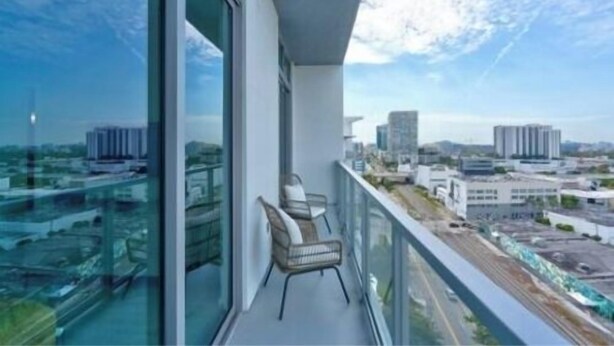 A balcony with a city view, a chair, and a glass railing. - Luxury 1 Bedroom Condo with Free Parking (Miami)