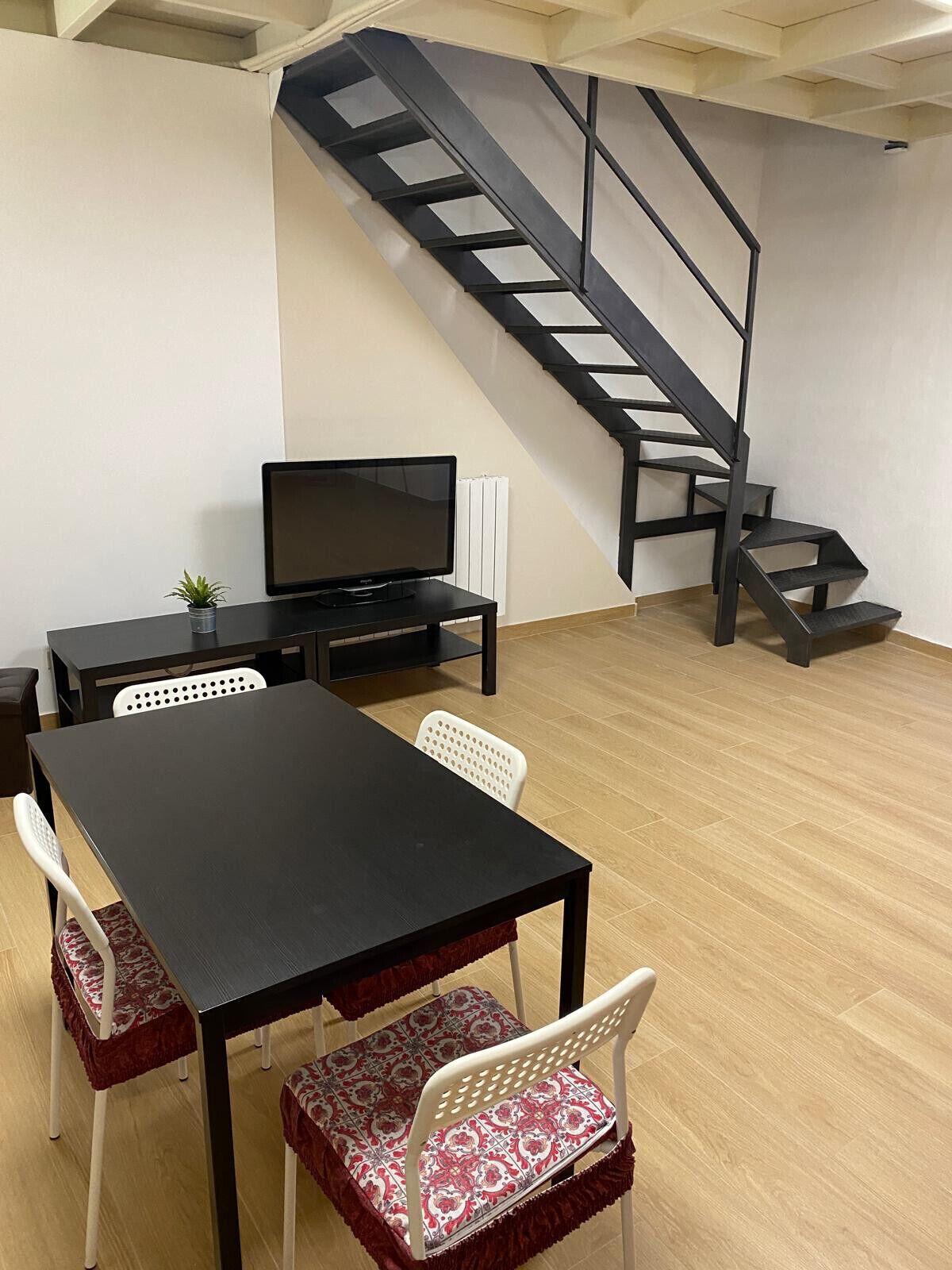 Ein Zimmer mit einem schwarzen Tisch, weißen Stühlen, einem Fernseher und einer Treppe.