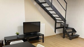Ein Zimmer mit einem schwarzen Tisch, weißen Stühlen, einem Fernseher und einer Treppe.