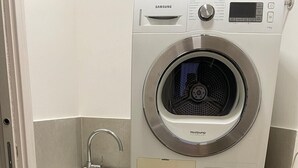 Ein kleiner Waschraum mit einer übereinander gestapelten Waschmaschine und einem Trockner, einem Spülbecken und einem Schrank.