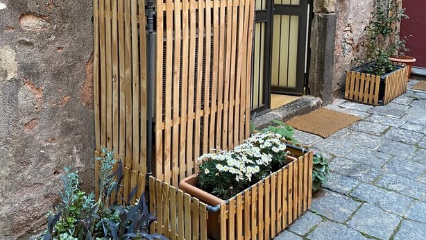 Ein hölzernes Tor, ein Blumentopf und ein pflastergelegter Innenhof.
