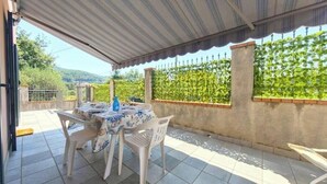 An outdoor patio with a table and chairs, a covered area, and a view of a vineyard. - Hostdomus - Azimut Apartment (Liguria)