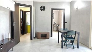 A modern living room with a dining area, a pet bed, and a clock on the wall. - Hostdomus - Azimut Apartment (Liguria)
