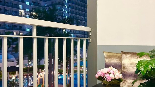 A balcony with a view of a cityscape at night, a small table with a potted plant, and a cushion on the wall. - Cozy 1-bedroom condo walking distance to MOA (Pasay City)