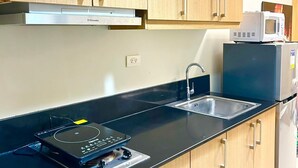 A modern kitchen with wooden cabinets, a black countertop, a built-in microwave, and a stove. - Cozy 1-bedroom condo walking distance to MOA (Pasay City)