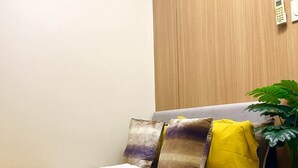 A bedroom with a bed, pillows, a bedside table, a plant, and a wall-mounted light switch. - Cozy 1-bedroom condo walking distance to MOA (Pasay City)