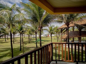 A view from a balcony overlooking a lawn with palm trees, a beach, and a building with a tiled roof. - Makai Resort All Inclusive (Aracaju)