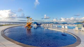 A circular infinity pool with a slide and a children's play area, surrounded by lounge chairs and umbrellas.