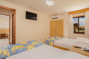 A hotel room with two beds, a TV, an air conditioning unit, and a view of the outside.