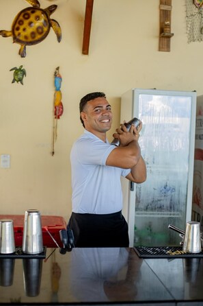 A person preparing a drink at a bar with a refrigerator and decorative elements in the background.