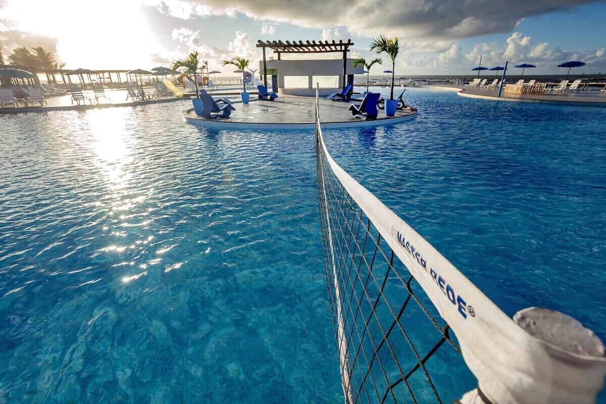 A clear blue pool with lounge chairs and umbrellas, a pergola, and a view of the ocean.