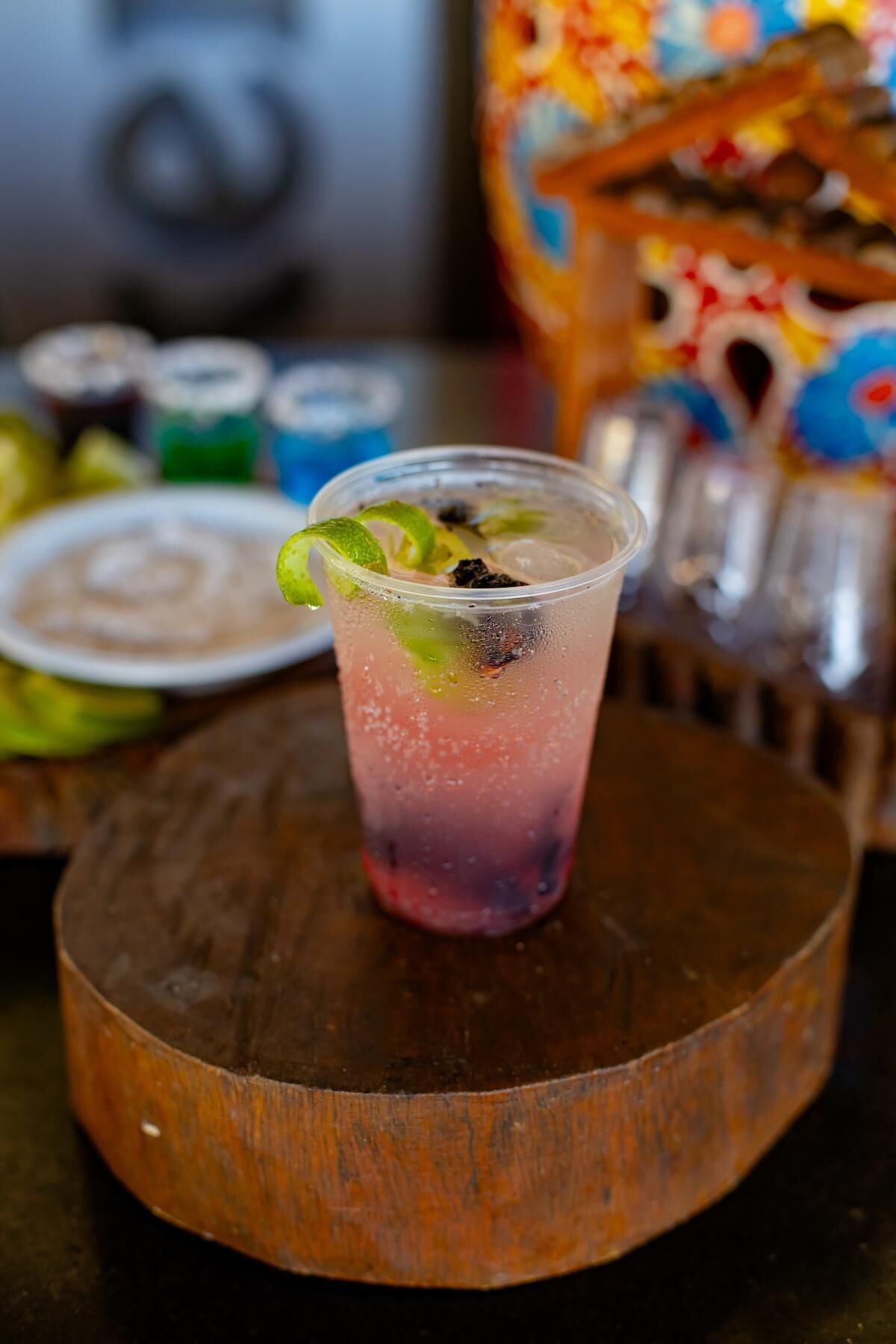 A drink with lime garnish on a wooden coaster.