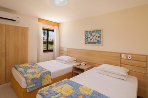 A hotel room with two beds, a wooden wardrobe, a window with curtains, and a wall-mounted artwork.