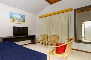 A hotel room with a bed, a TV, two wicker chairs, a large mirror, and a painting on the wall. - Makai Resort All Inclusive (Aracaju)