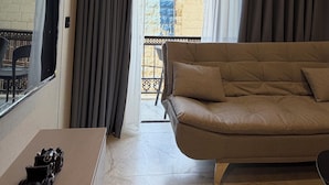 Un salon avec un canapé, un téléviseur et un balcon doté de rideaux.