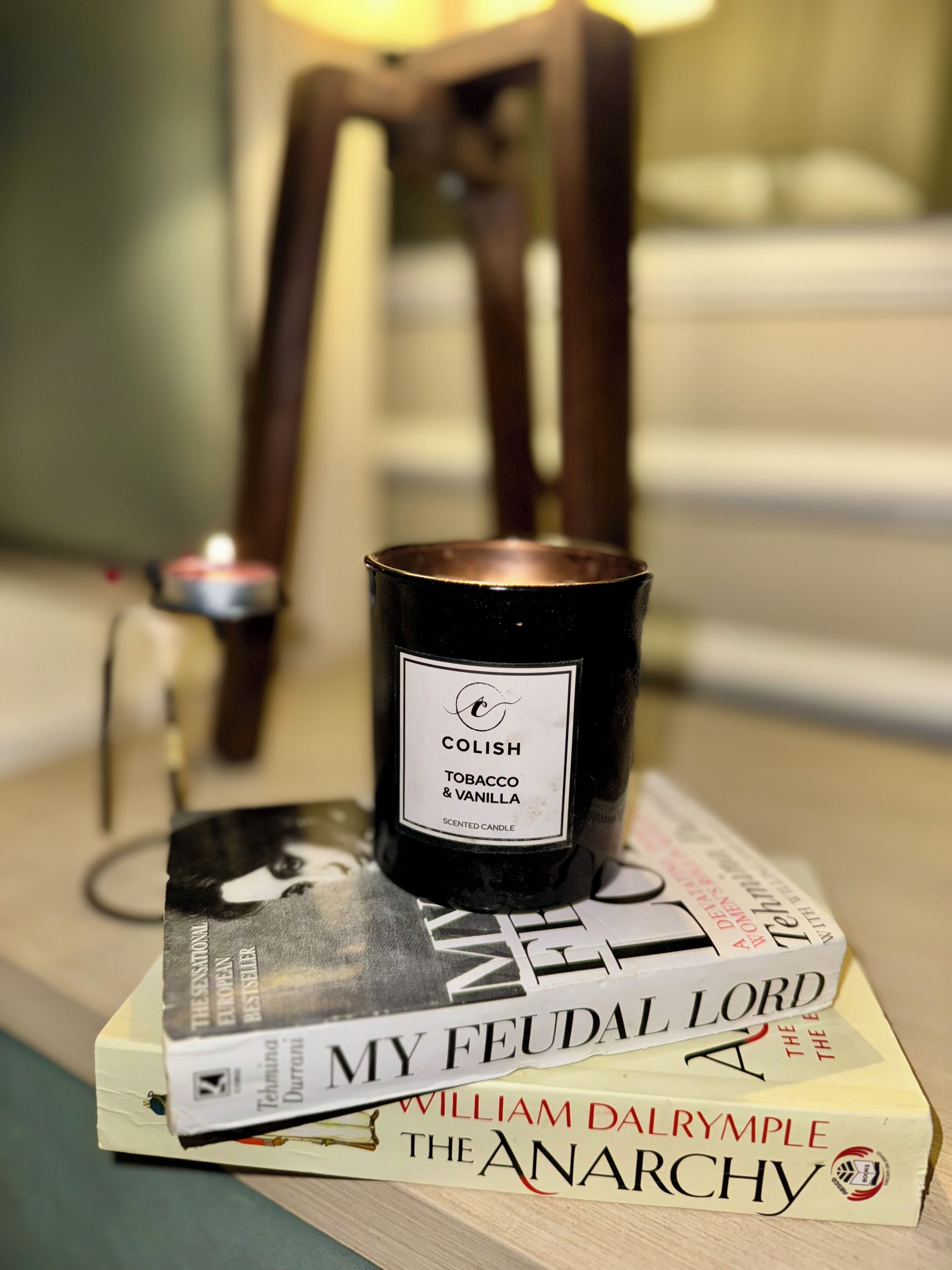 A scented candle labeled 'Colish Tobacco & Vanilla' on a stack of books.