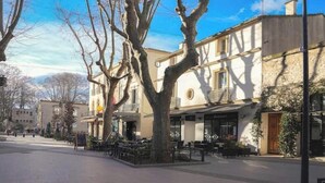 Un immeuble avec un café au rez-de-chaussée, des tables à l’extérieur et un arbre devant.