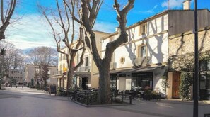 Un immeuble avec un café au rez-de-chauss ée, des tables à l’extérieur et un arbre devant.