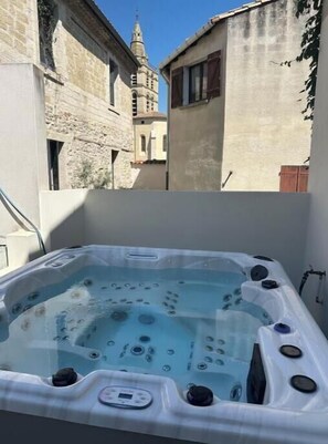 Un bain à remous doté d’un panneau de commande, entouré de bâtiments en pierre et sous un ciel dégagé.