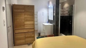 Une chambre à coucher avec un lit, une armoire en bois, une salle de bain avec un lavabo et une douche.