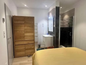 Une chambre à coucher avec un lit, une armoire en bois, une salle de bain avec un lavabo et une douche.