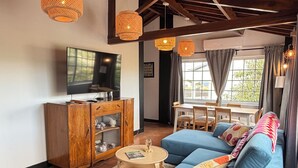 Sala de estar com sofá azul, armário de madeira, televisão e luminárias de vime suspensas.