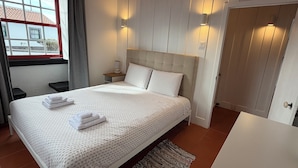 Cama bem arrumada com toalhas, mesa de cabeceira com abajur e vista para o exterior através de uma janela.