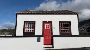 Um edifício branco com porta e janelas vermelhas, telhado de telhas e um pequeno degrau para a entrada.
