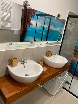 Ein Badezimmer mit zwei Waschbecken, einem Spiegel und einer Duschkabine aus Glas.