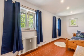 A bedroom with a bed, a window with curtains, a radiator, and a small window with a view of greenery. - Room 'Magic 3' in Dischingen (Dischingen)