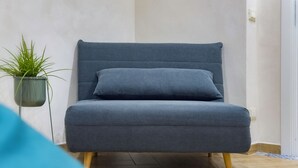 Ein graues Sofa mit Holzbeinen, ein Blumentopf und ein Fliesenboden.
