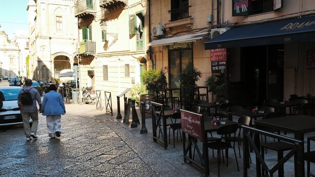 Eine Straße mit Außenbestuhlung, ein Restaurant mit italienischer Beschilderung und ein Gebäude mit Balkon.