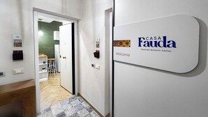 Ein Flur mit einem 'CASA Fauda'-Schild, einer Tür zu einem Zimmer und einem gemusterten Teppich.