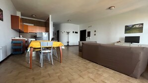 Una sala de estar con un sofá marrón, un comedor con mantel amarillo y una cocina con armarios de madera.