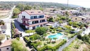 Un edificio residencial de varios pisos con piscina, rodeado de vegetación y otras casas.