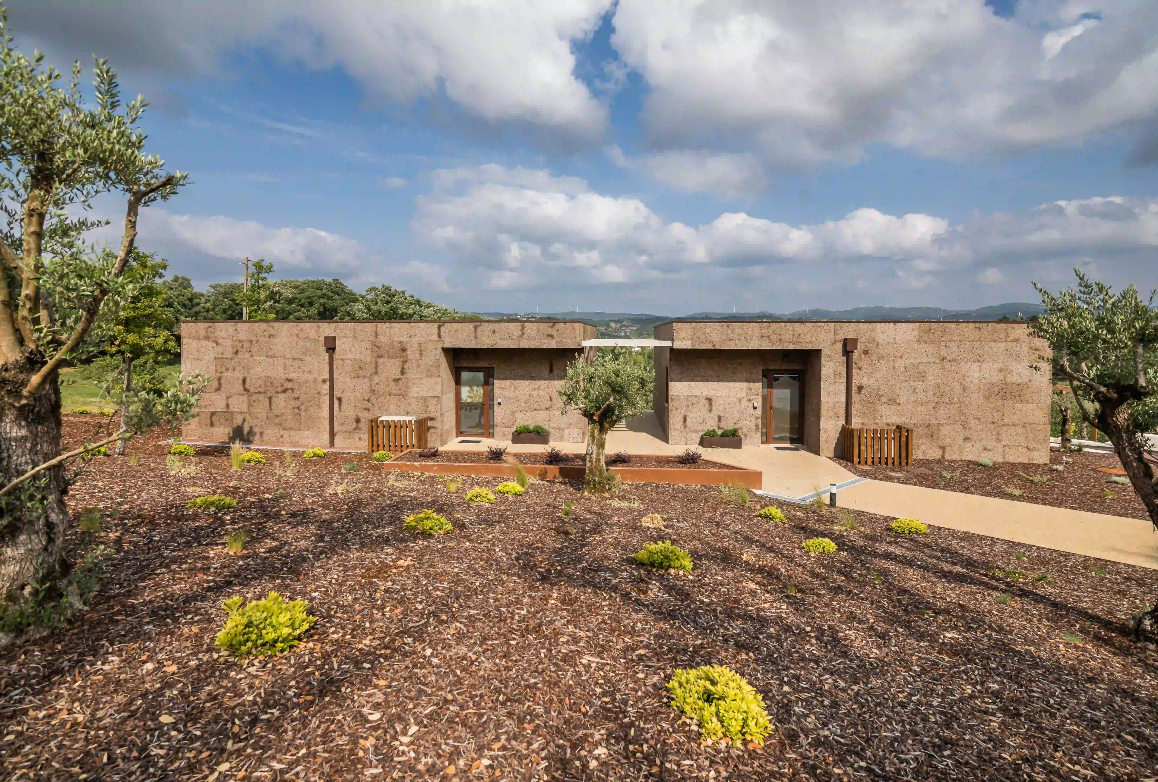A modern building with two symmetrical sections, a landscaped garden with mulch and small plants, and a clear sky.
