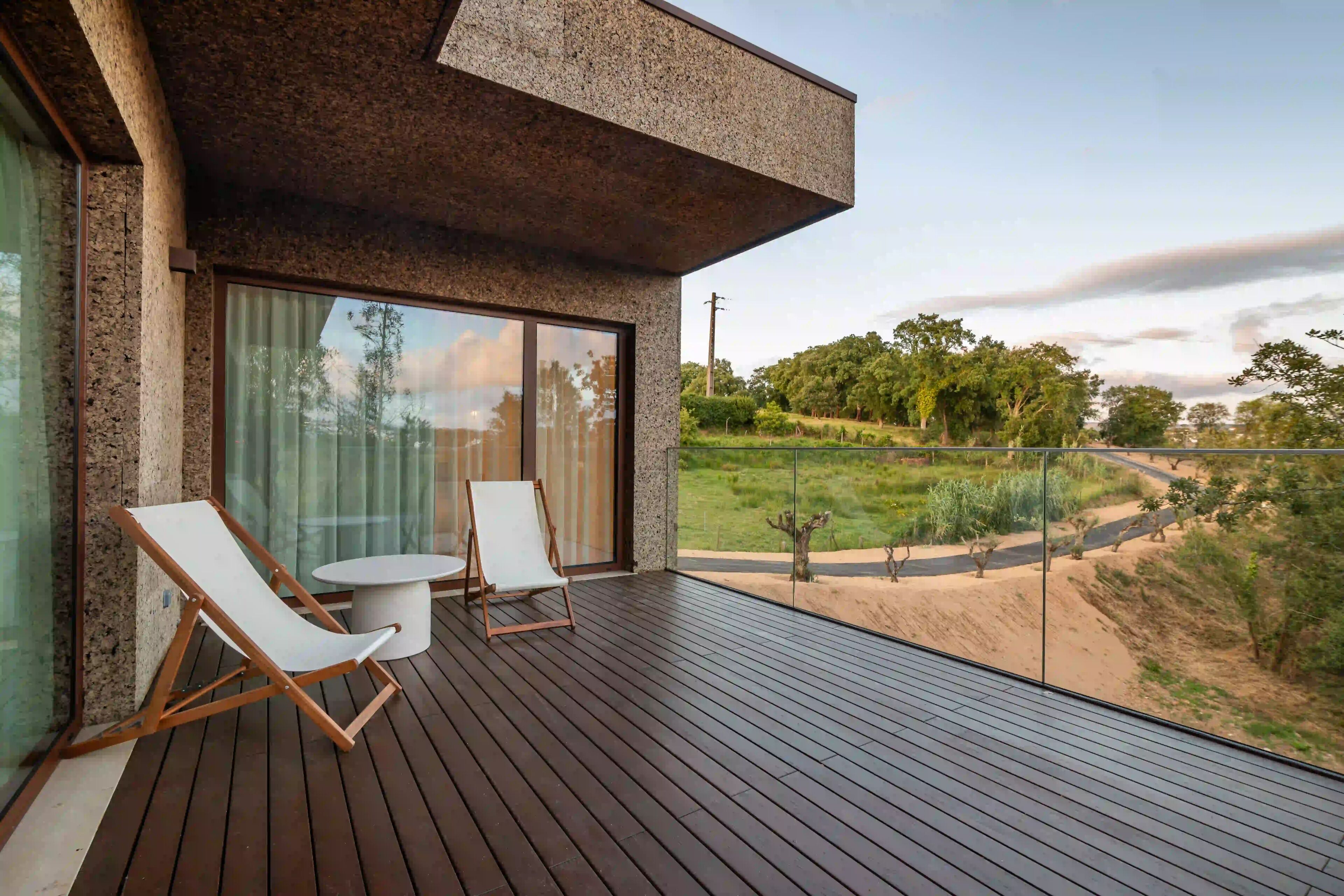 A modern outdoor deck with two lounge chairs and a small table, overlooking a landscaped garden.