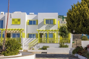 Un edificio moderno con paredes blancas y detalles amarillos, que cuenta con balcones y una escalera que conduce a la entrada.