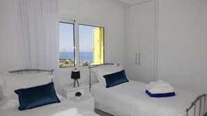 A hotel room with two beds, a window with a view of the sea, a bedside table with a lamp, and a wardrobe. - Yellow 16 Sea View Vacation Home (Paphos)