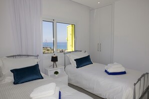 Una habitación de hotel con dos camas, una ventana con vistas al mar, una mesita de noche con una lámpara y un armario.