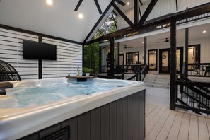 Ein Whirlpool mit Holzterrasse, ein an der Wand befestigter Fernseher und eine Treppe zu einer oberen Ebene.