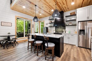 Eine moderne Küche mit Holzboden, Barhocker, Edelstahlgeräten und Blick ins Freie.