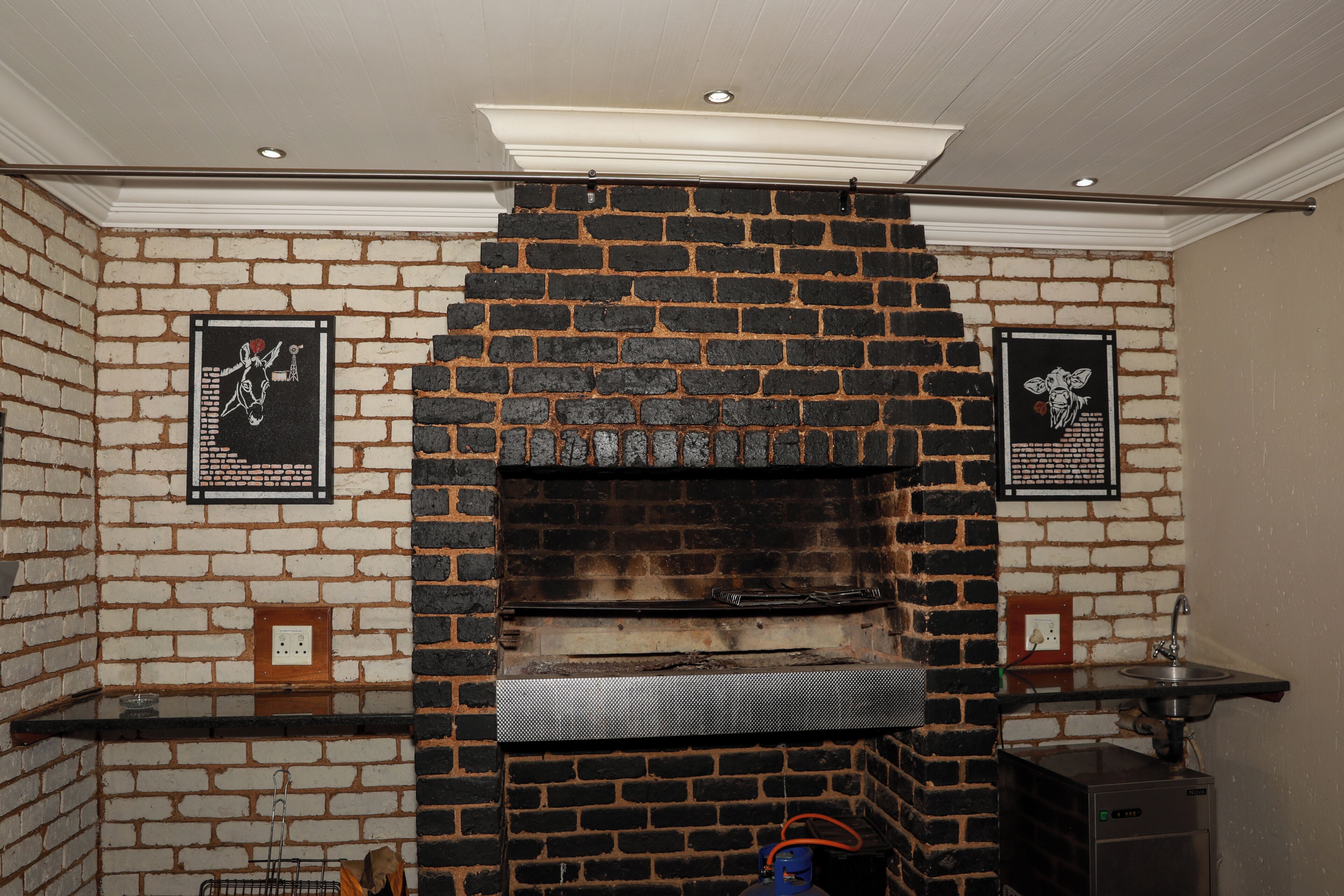 Un four en briques avec une étagère en métal, un luminaire fixé au mur et deux tableaux encadrés.