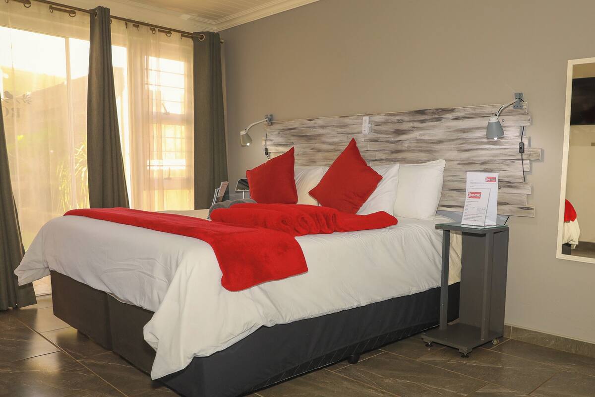 A hotel room with a bed, a nightstand, a lamp, and a mirror.