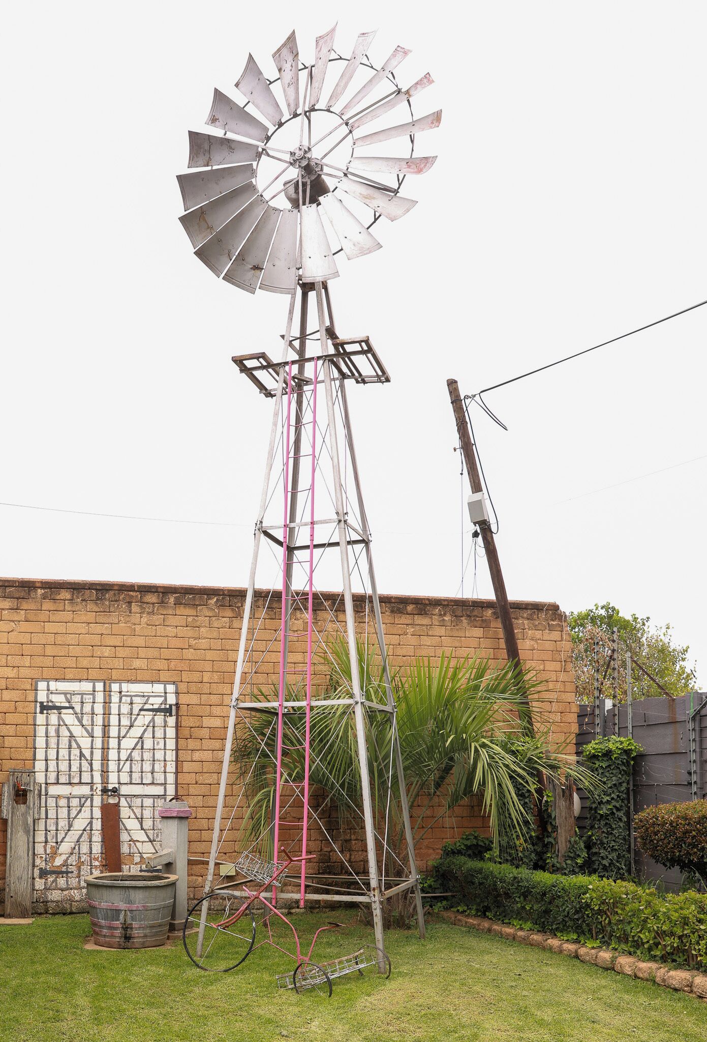 Een windmolen met een metalen constructie, een bakstenen muur en een kleine tuin met een fiets.