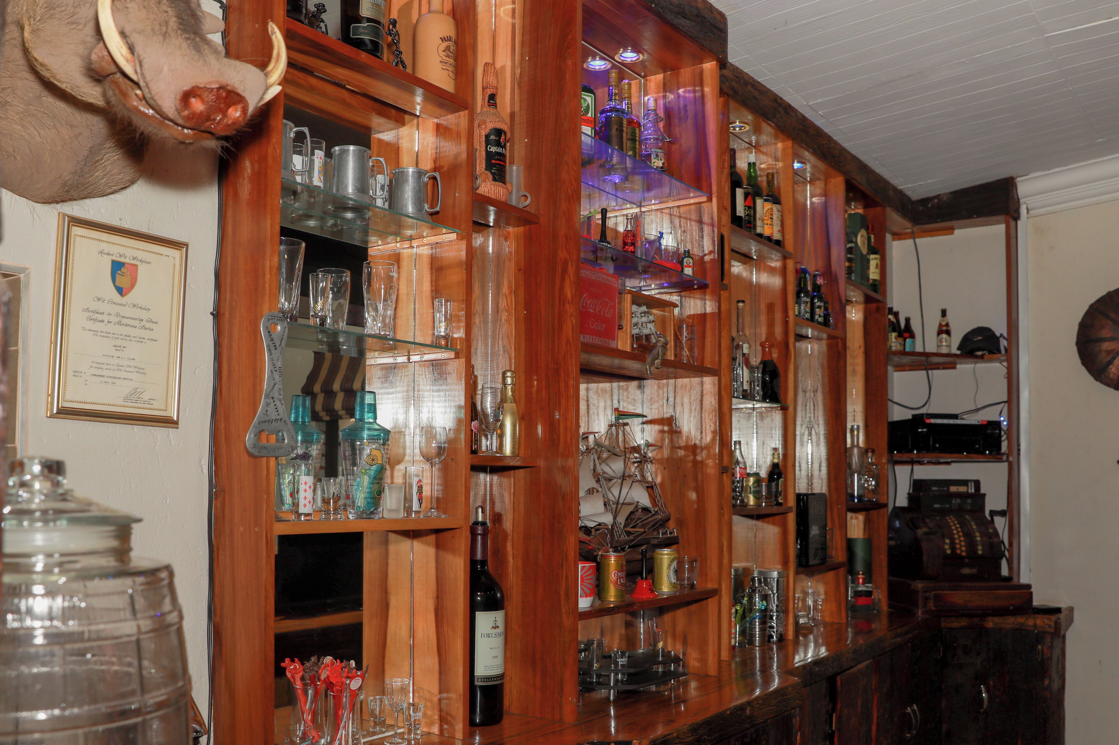 A bar with wooden shelves stocked with bottles, glasses, and a large jar.