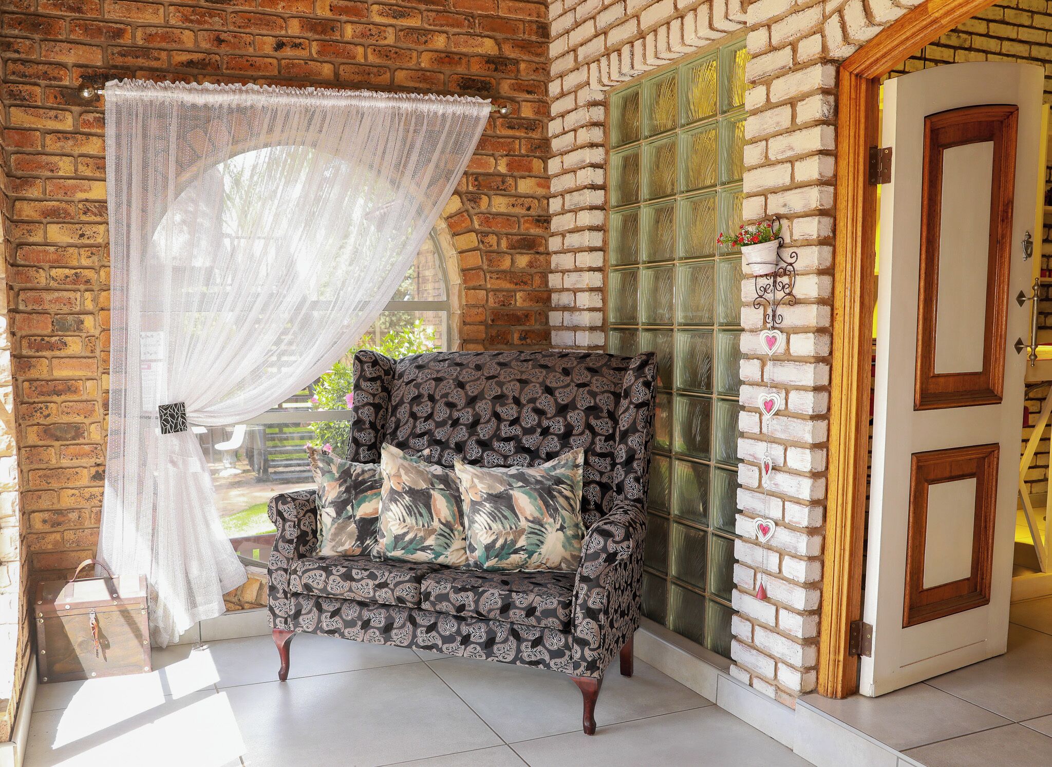 A room with a brick wall, a patterned armchair, a white curtain, and a glass door.