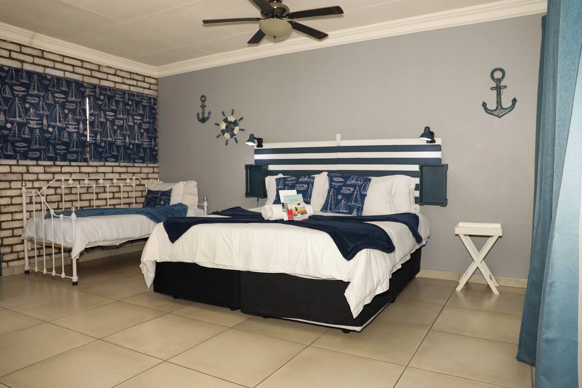 A bedroom with two beds, a ceiling fan, a brick-patterned wall, and nautical-themed decor.