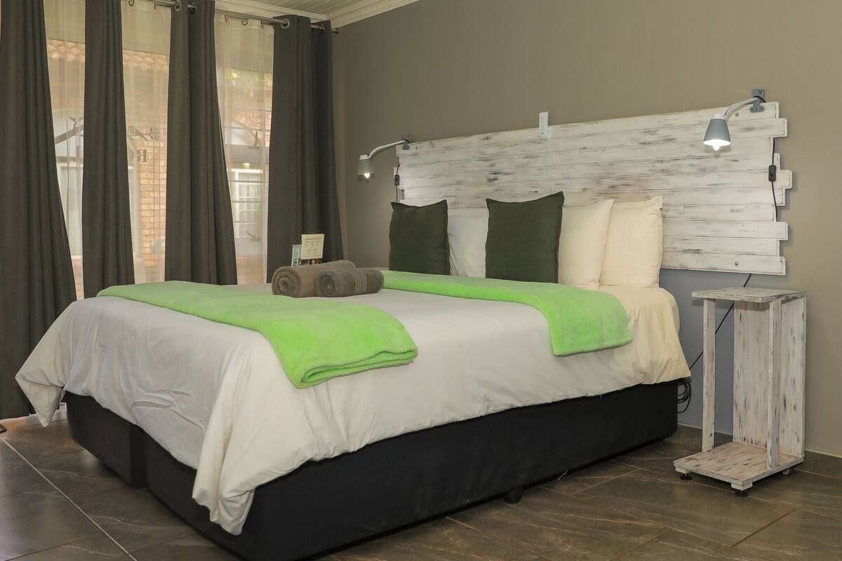 A bed with a white and green bedspread, a headboard with multiple pillows, and a bedside table with a lamp.